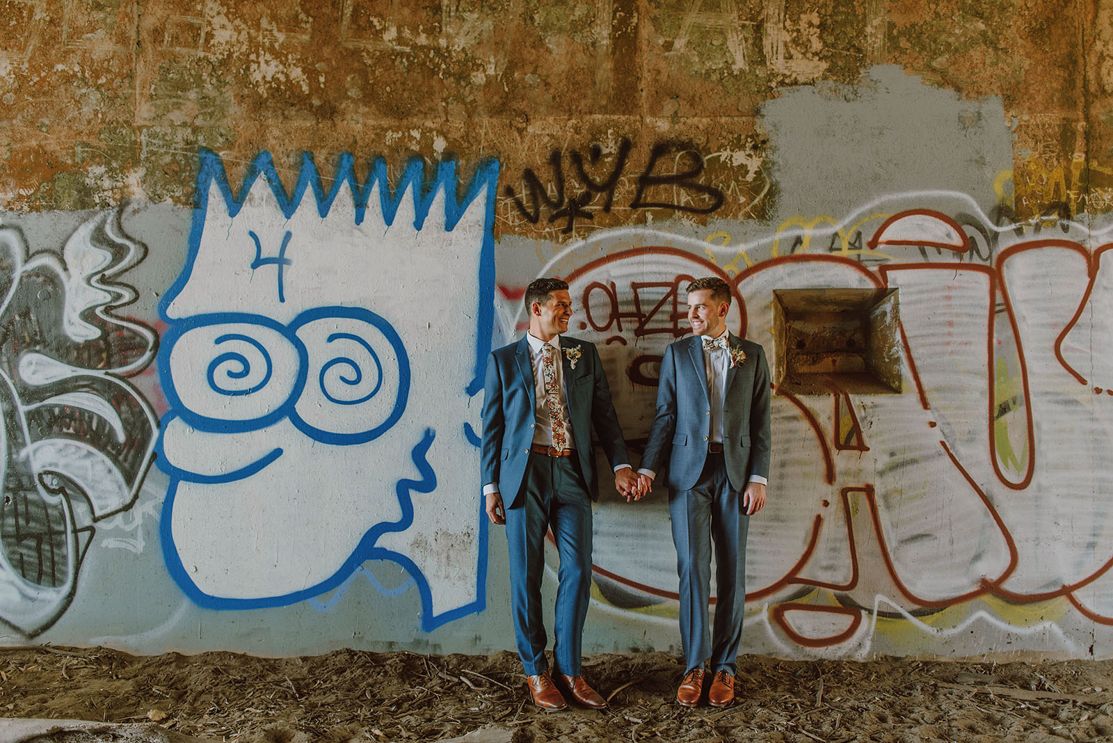 Grooms leaning against a graffiti wall at Fort Funston - Foreign Cinema Wedding
