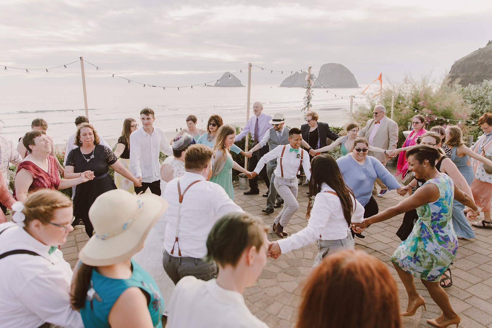 Overhead shot of guests dancing in a circle during the hora - Oceanside Community Club Wedding on the Oregon Coast” title=